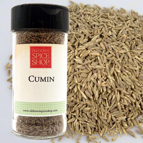 Jar of cumin seeds from Old Town Spice Shop with scattered cumin seeds on a white background