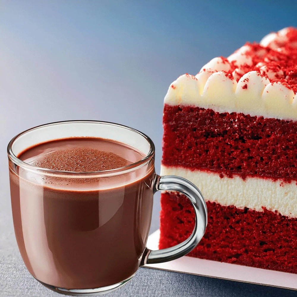 Glass mug of hot chocolate next to a slice of red velvet cake on a light blue background
