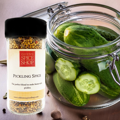 Jar of pickling cucumbers with a container of Old Town Spice Shop pickling spice on a wooden surface.