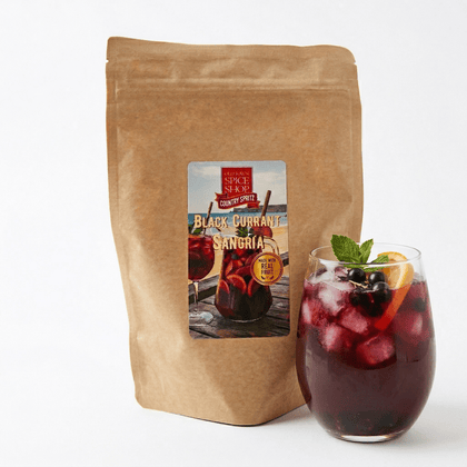 Kraft paper bag of Country Spice Black Currant Sangria with a glass of sangria on a white background