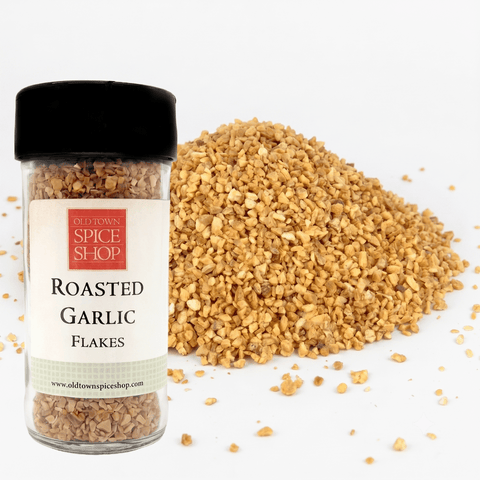 Jar of roasted garlic flakes from Old Town Spice Shop with scattered flakes on a white background