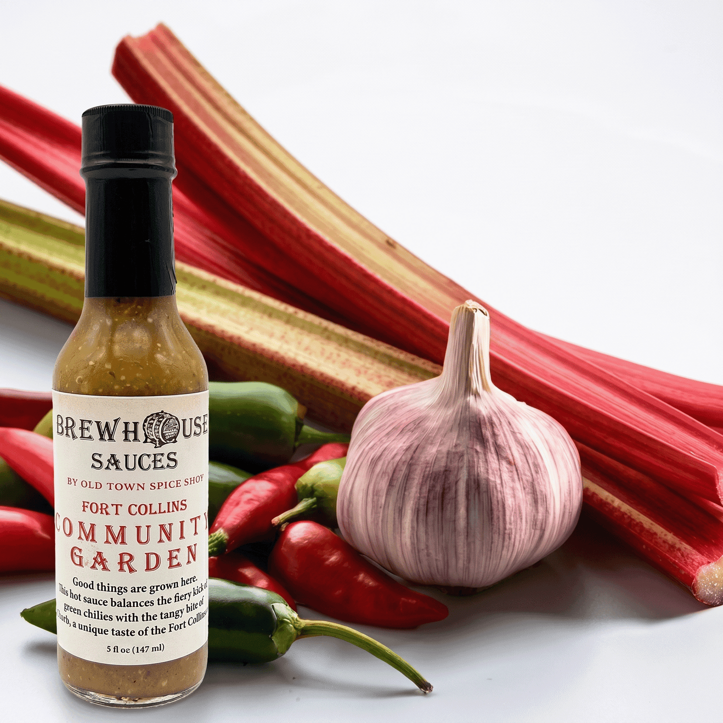 Bottle of Brewhouse Sauces Fort Collins Community Garden with garlic and rhubarb on a white background