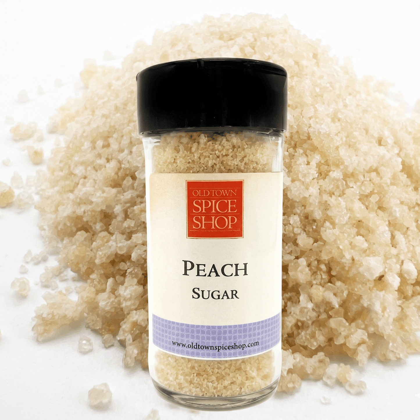 Bottle of Peach Sugar from Old Town Spice Shop surrounded by sugar crystals on a white background
