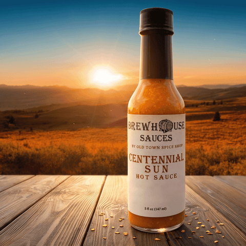 Bottle of Brewhouse Sauces Centennial Sun Hot Sauce on a wooden surface with a scenic background