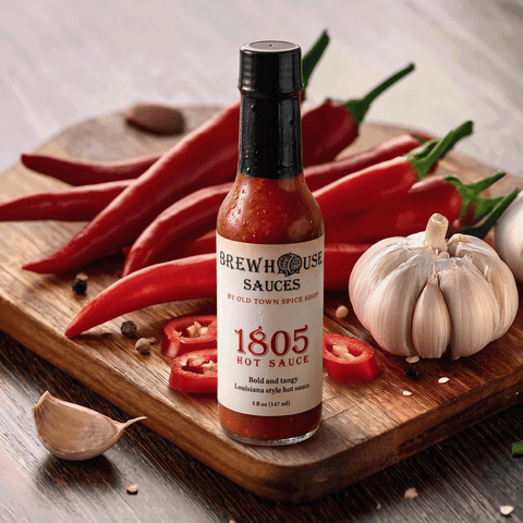 Bottle of Brewhouse Sauces 1805 Hot Sauce on a wooden cutting board with red peppers and garlic.