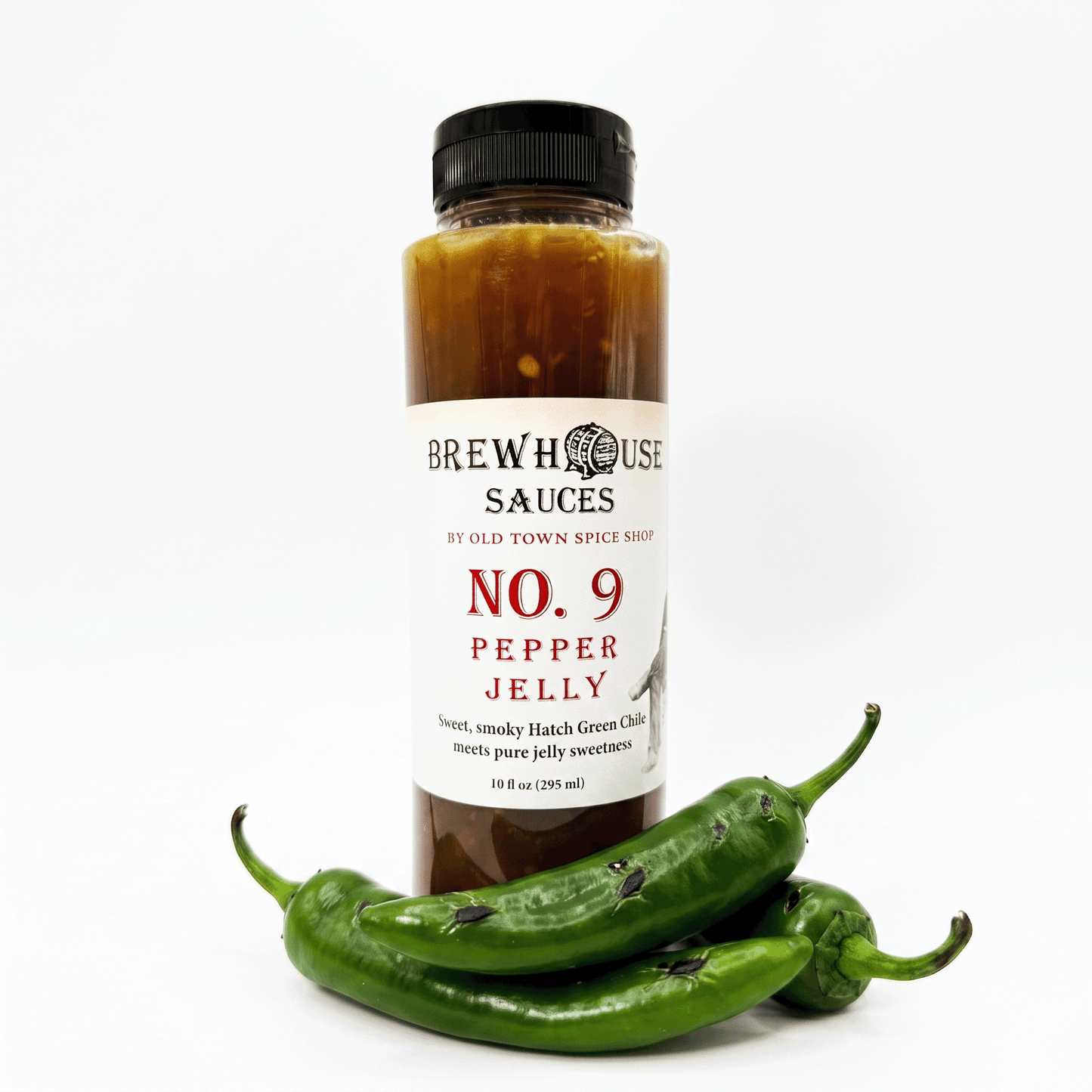 A bottle of Brewhouse Sauces No. 9 Pepper Jelly stands on a white background with three green chili peppers placed in front of the bottle.
