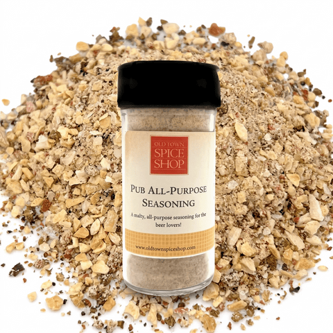 A bottle of Old Town Spice Shop Pub All-Purpose Seasoning stands centered in front of a pile of coarse seasoned salt pieces on a white background.