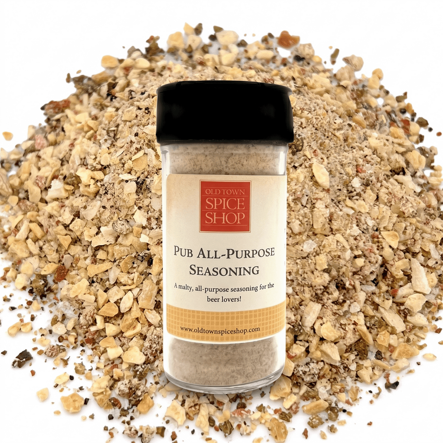A bottle of Old Town Spice Shop Pub All-Purpose Seasoning stands centered in front of a pile of coarse seasoned salt pieces on a white background.