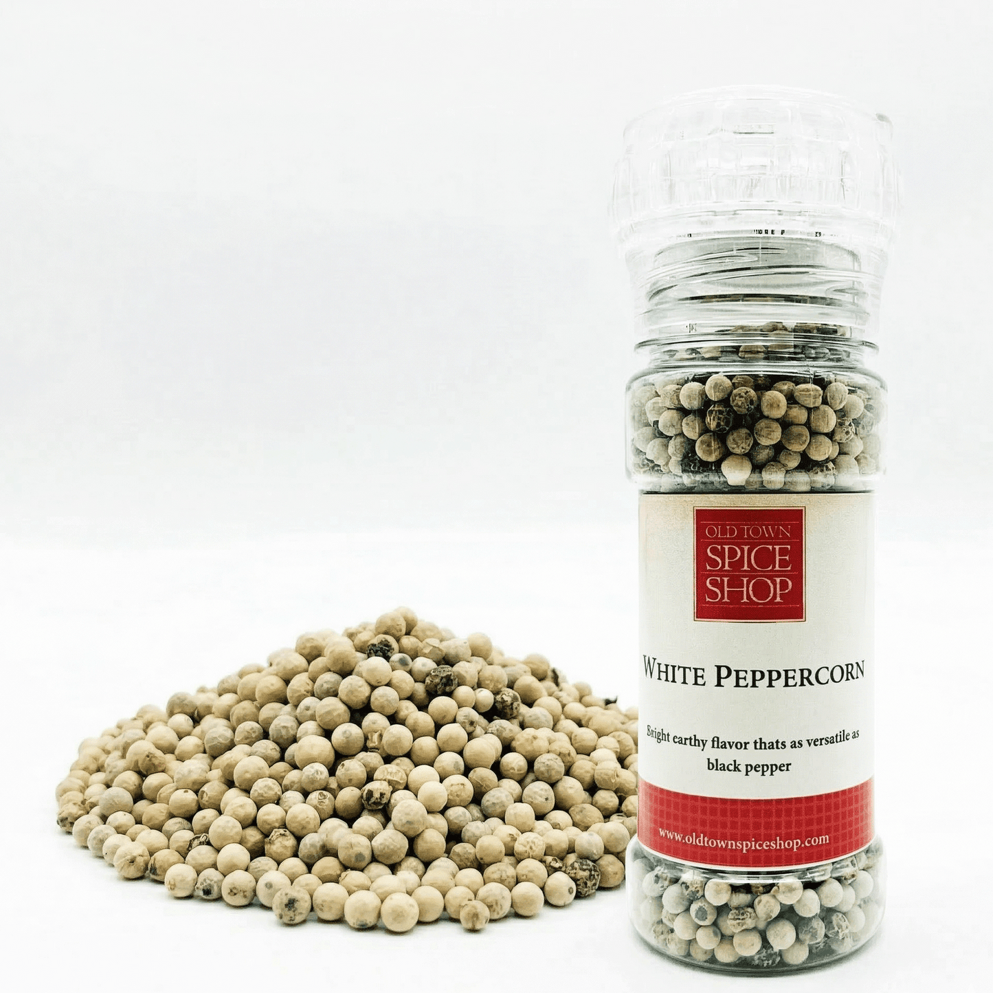 Bottle of white peppercorns from Old Town Spice Shop with a pile of peppercorns on a white background