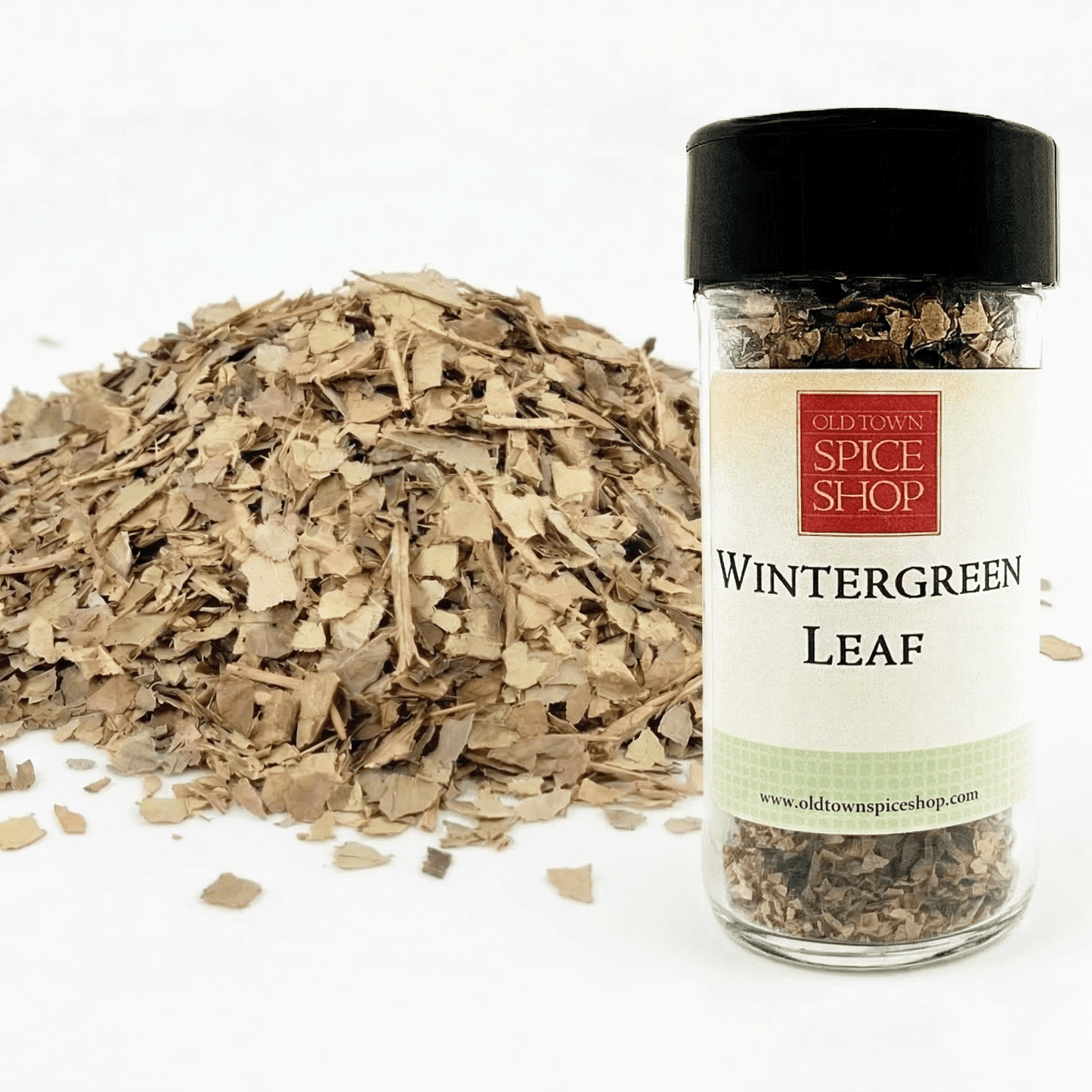 Jar of wintergreen leaf from Old Town Spice Shop with a pile of dried leaves on a white background