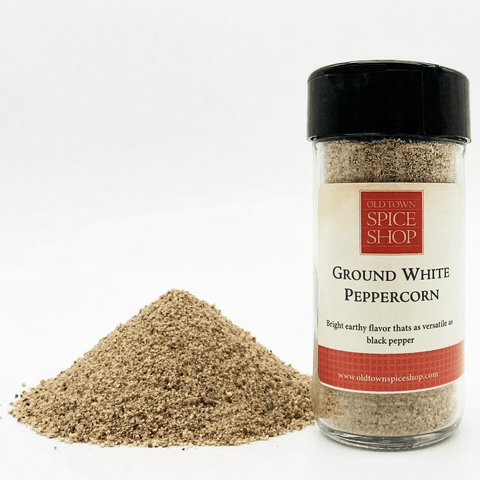 Bottle of ground white peppercorn with a pile of peppercorns on a white background