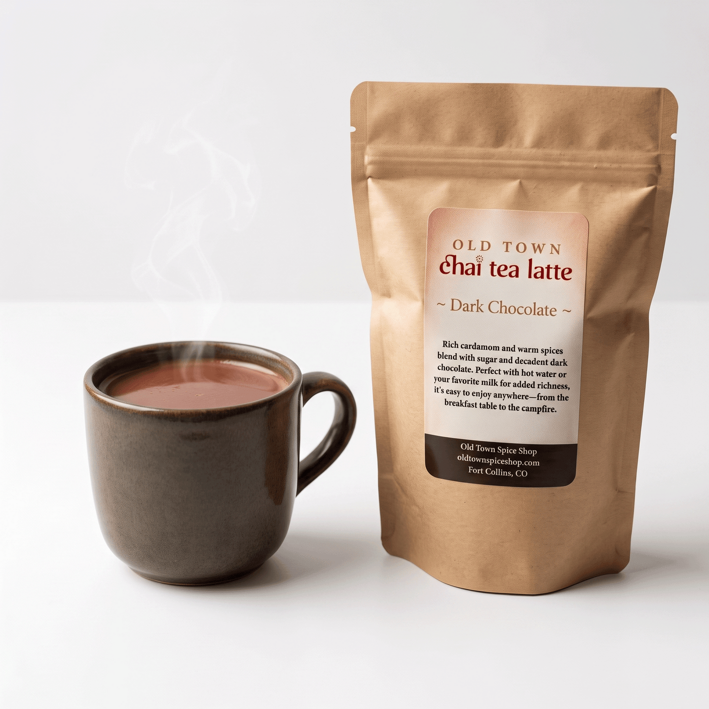A kraft paper stand-up pouch of Old Town Chai Tea Latte Dark Chocolate next to a dark ceramic mug filled with steaming chai tea, on a clean white background.