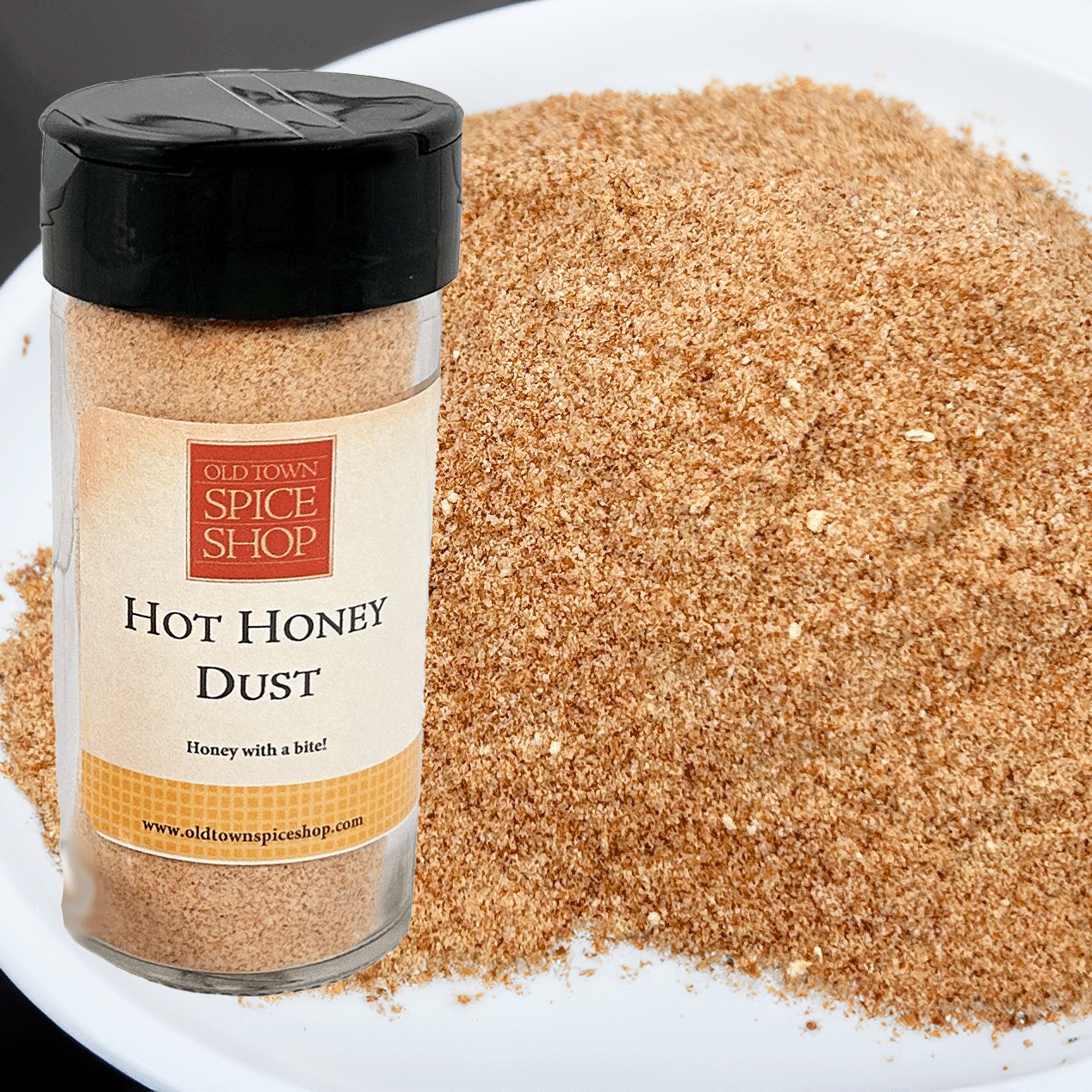 Jar of Old Town Spice Shop Hot Honey Dust with a white plate of honey dust in the background.
