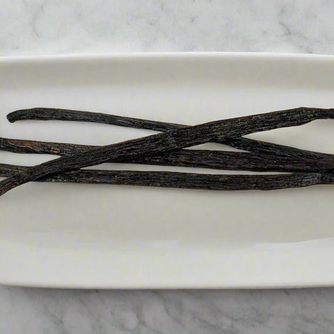 Three vanilla beans on a white marble surface