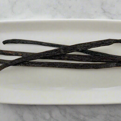 Three vanilla beans on a white marble surface